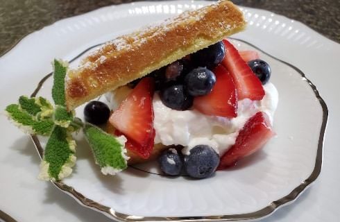 Sliced strawberries and blueberries on whipped cream with dusted waffle on top