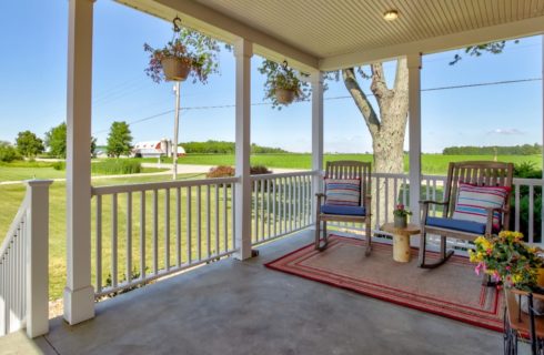 Front porch of property with two wooden rockers, area rug, and hanging flower baskets