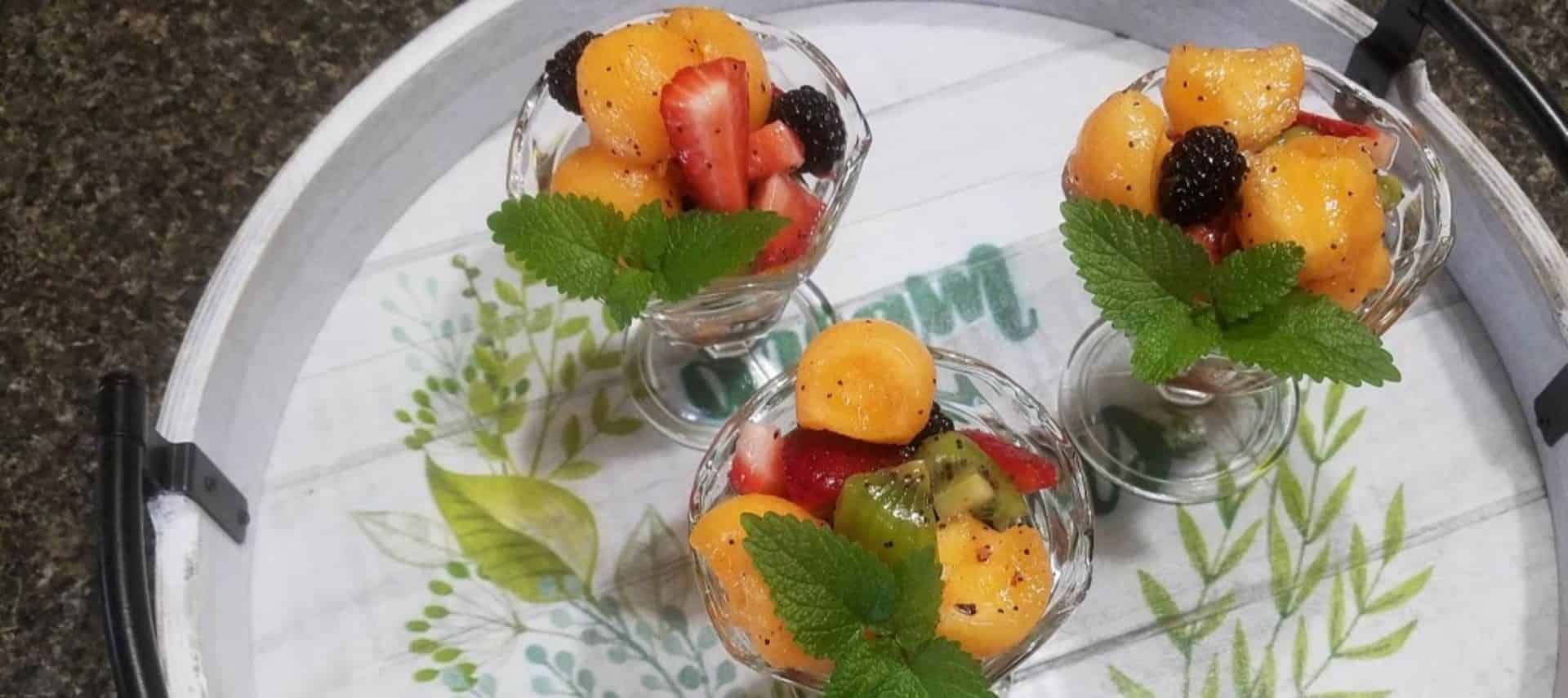 Three glass fruit cups filled with melon balls, sliced strawberries, blackberries, and kiwi