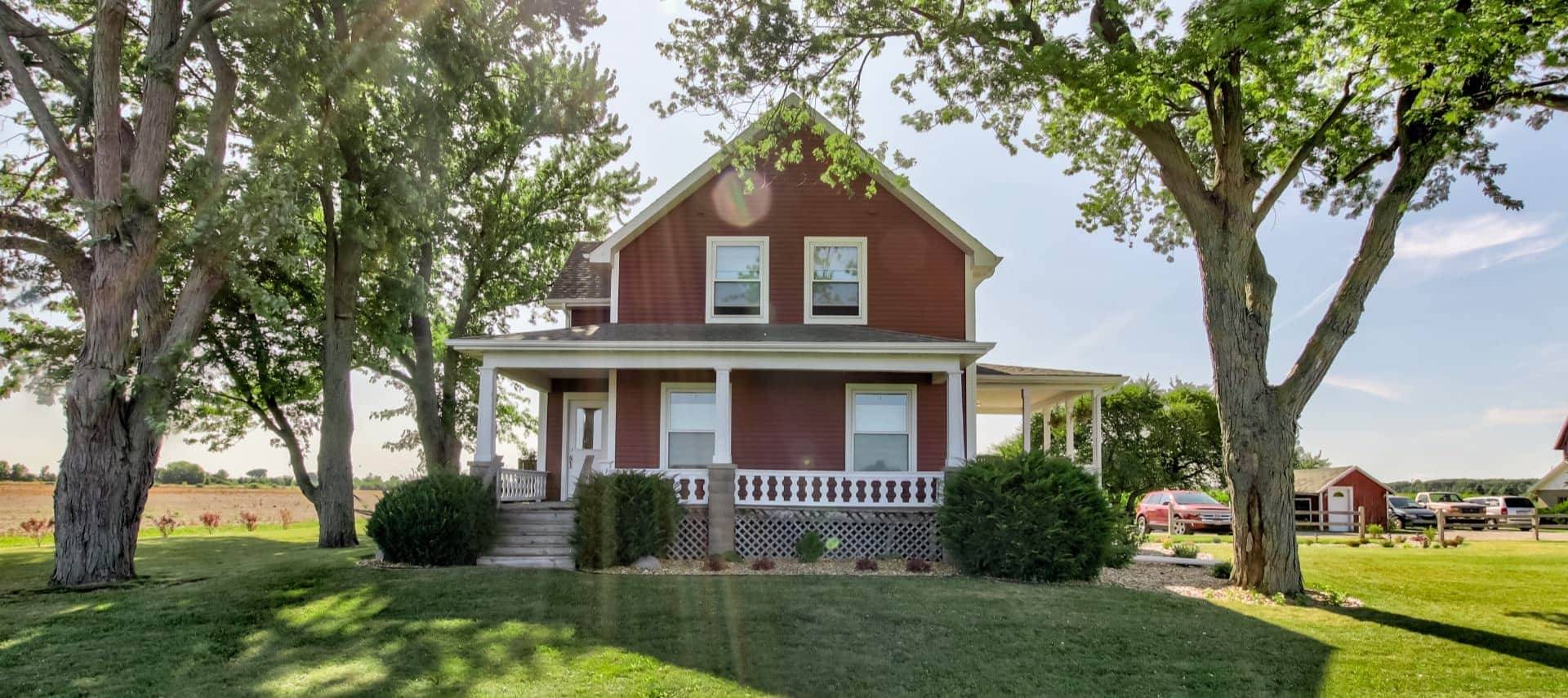 Front exterior view of the property painted burgundy with white trim surrounded by green grass and tall trees