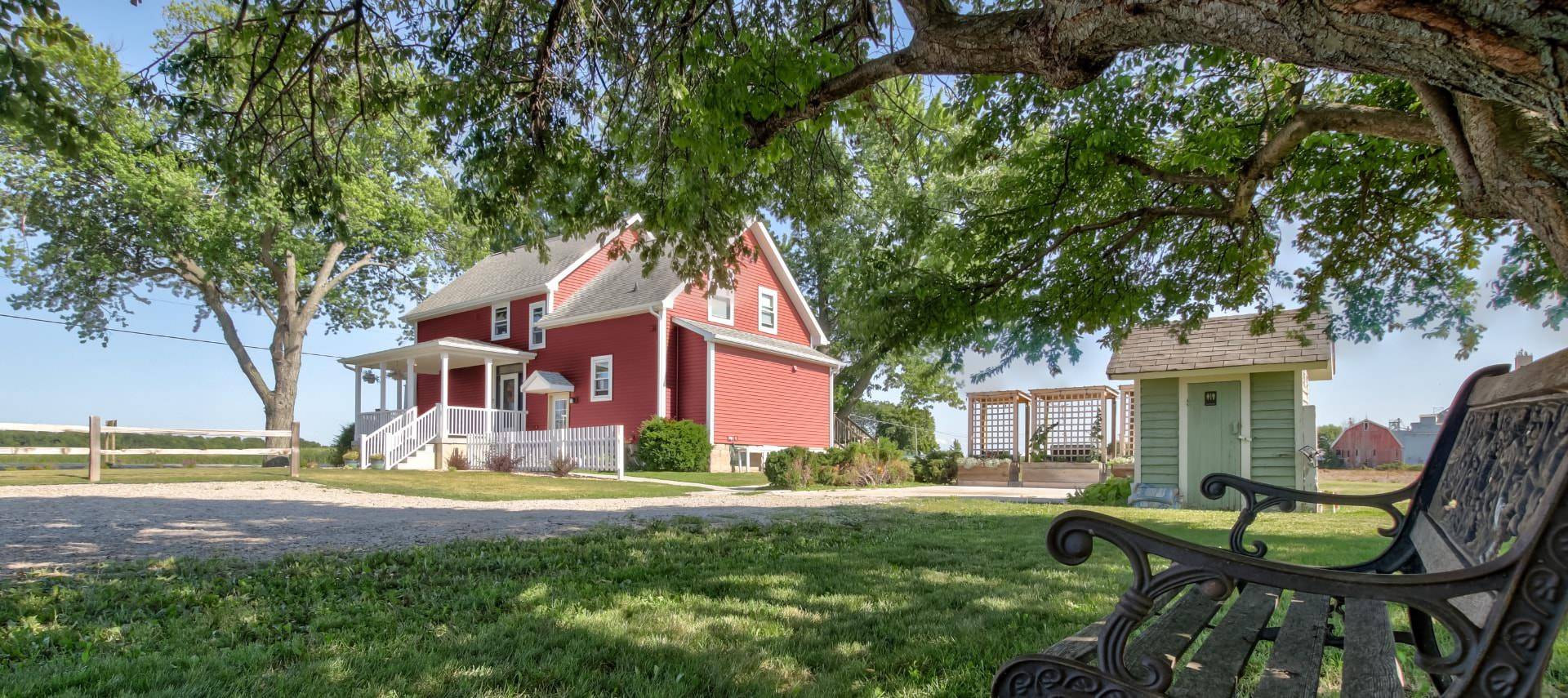 Front exterior view of the property painted burgundy with white trim surrounded by green grass and tall trees