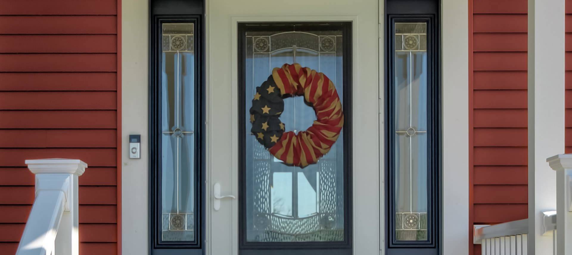 Exterior view of property's front door painted white with navy trim and wreath decorated with American flag fabric